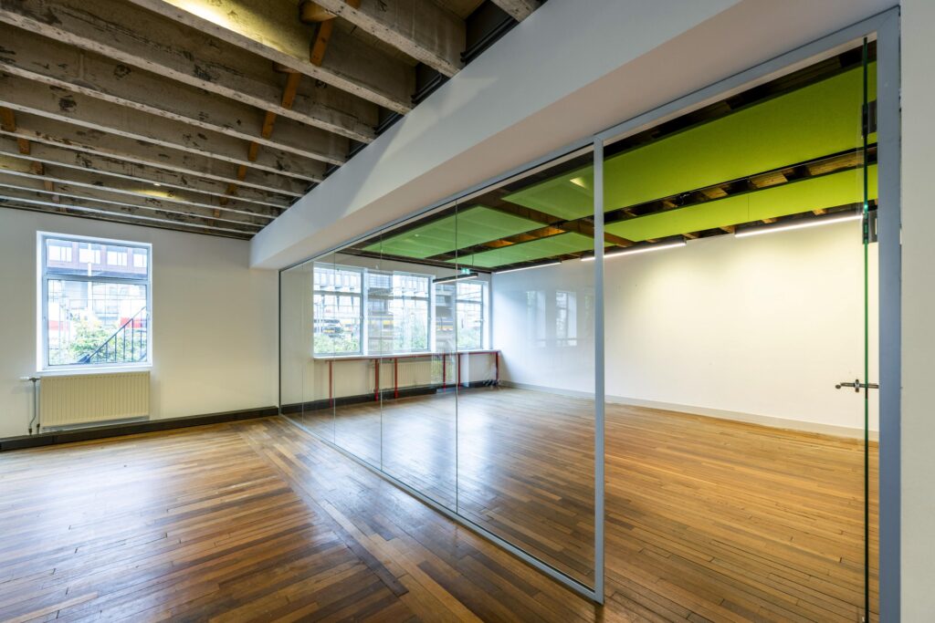 Licht en modern kantoorinterieur aan de De Ruijterkade met houten vloer, glazen wand en zichtbare plafonddragers.